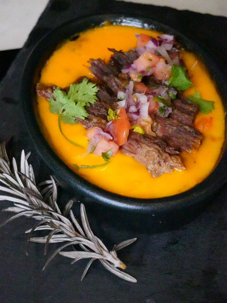 A black bowl filled with orange soup, topped with meat and herbs.